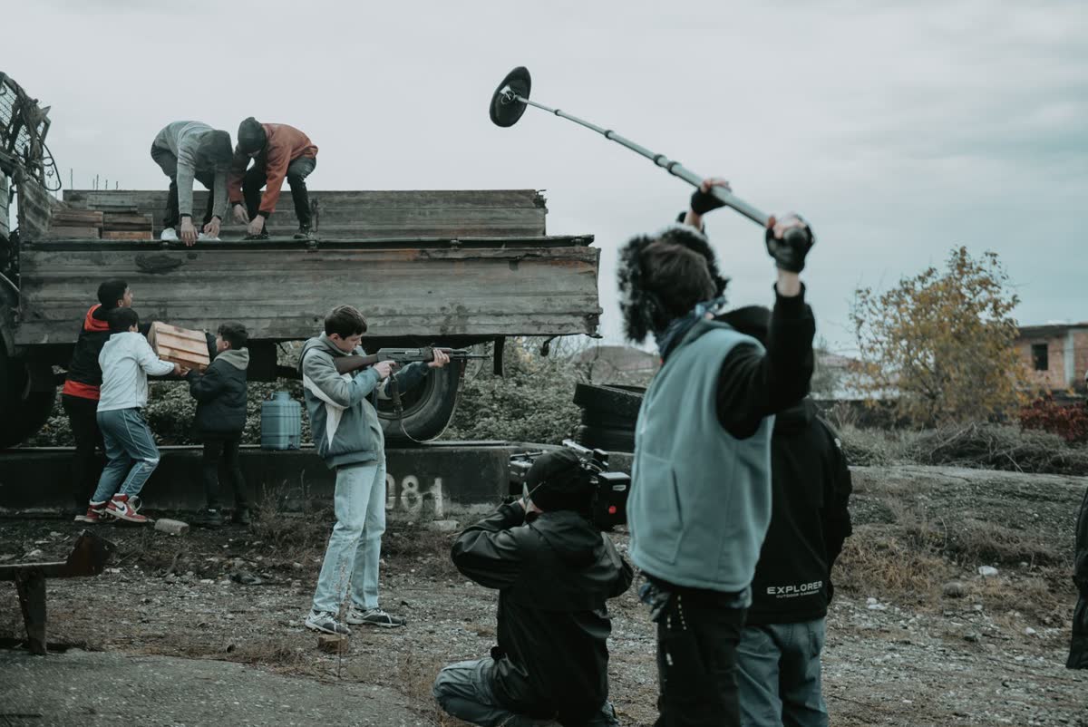 A film crew with a boom microphone and camera working outdoors beside a truck