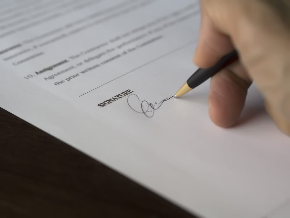 A hand signing a paper document with a fountain pen